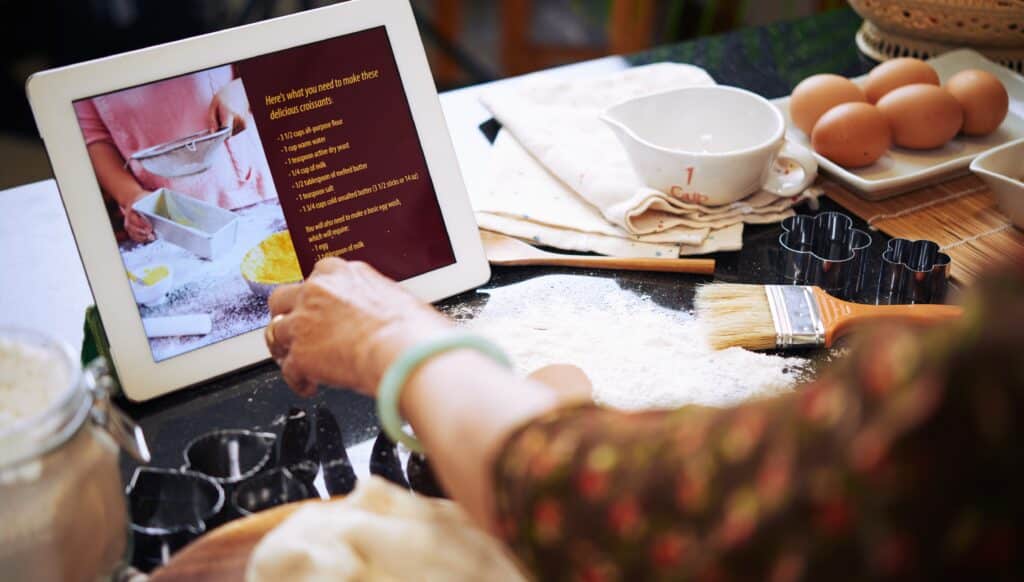 A tablet displaying a digital recipe layout is placed on a kitchen counter while someone follows it to bake, illustrating user-friendly web design in food and recipe websites.