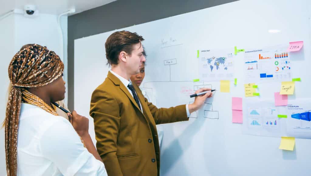 A diverse team collaborates on project management tasks, using colourful sticky notes and a large paper layout to map strategies and timelines during a planning session.