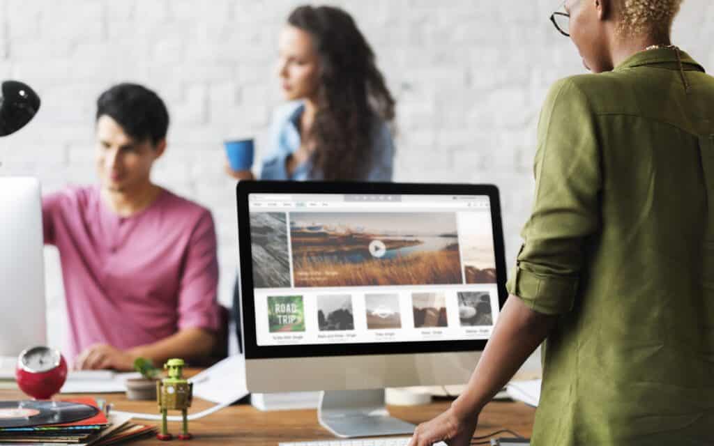 A creative team collaborates in a modern office while one member previews a website interface on a desktop screen, illustrating teamwork in professional web design development.