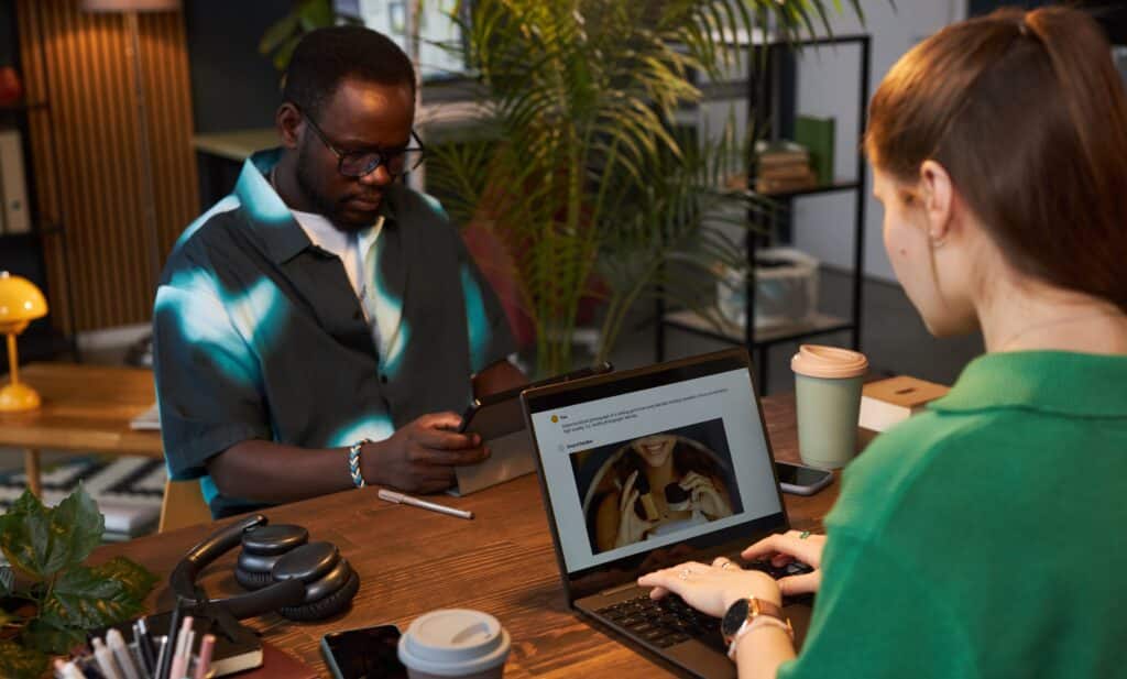Two professionals working at a shared desk in a modern office, with one woman optimising product content on her laptop—representing creative digital strategies for SEO Auckland campaigns.