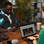Two professionals working at a shared desk in a modern office, with one woman optimising product content on her laptop—representing creative digital strategies for SEO Auckland campaigns.